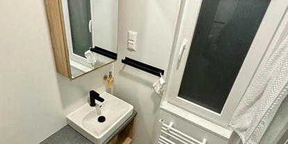 Hundehotel - Garten - Österreich - Im Badezimmer befinden sich ein Spiegelschrank, Fön und ein Heizkörper für Handtücher. - Blue Flamingo Lake Lodge 