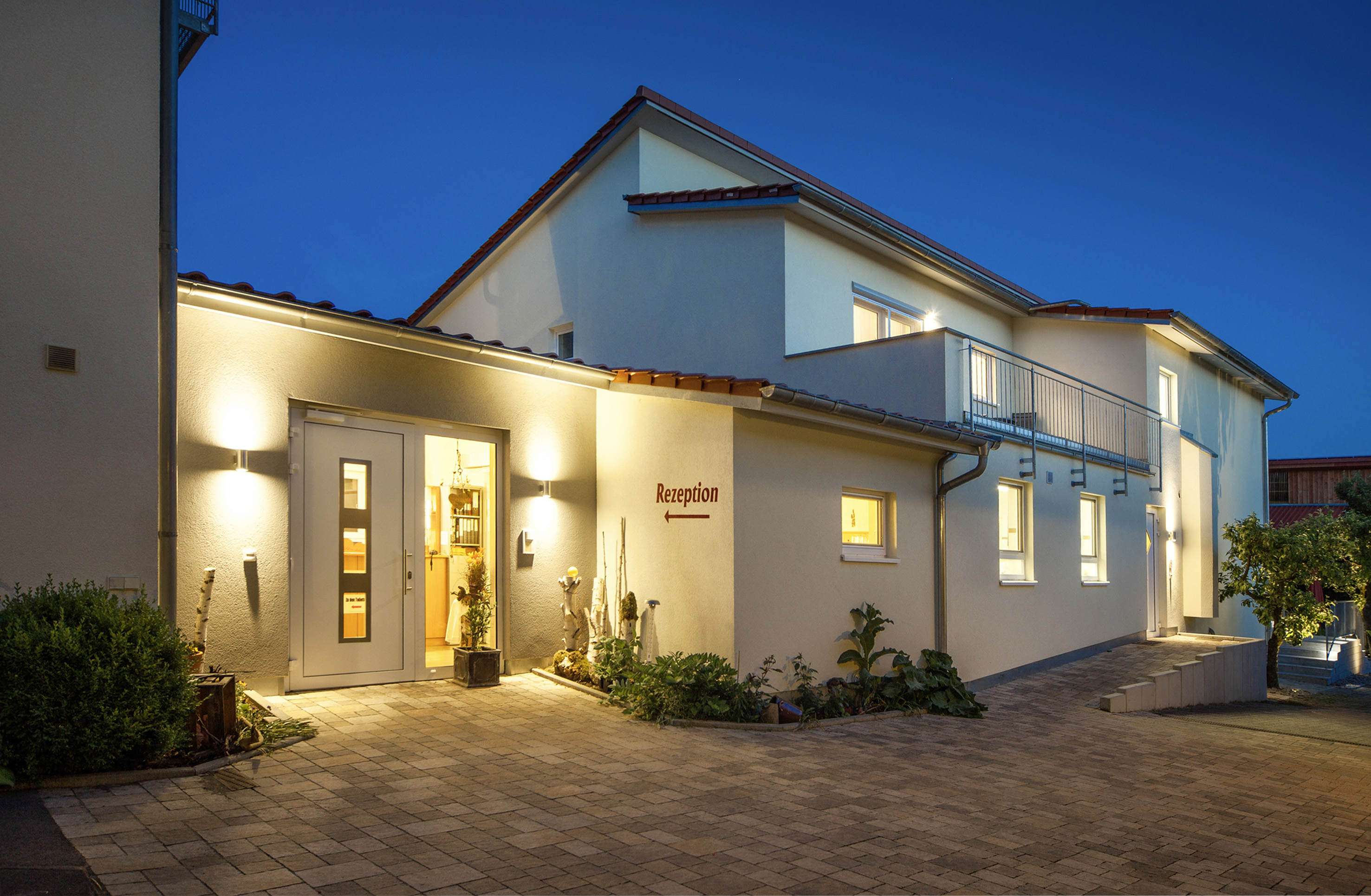 Hundehotel - Dogsitting - Blick in der Dämmerung über den Hof zum Eingang Rezeption der erleuchteten Pension Heuler - Gästehaus Pension Heuler